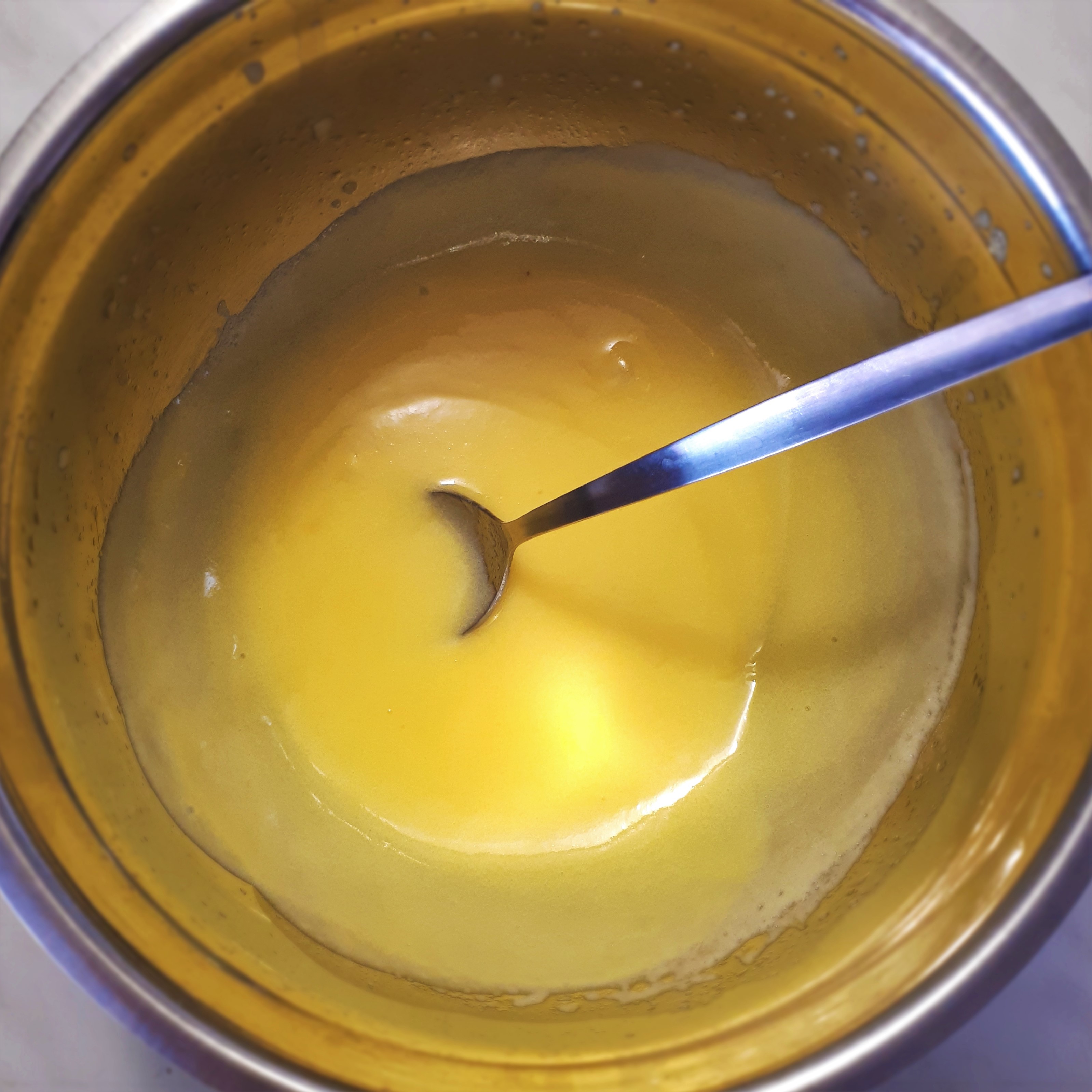 Hotový citrónový krém lemon curd v antikorovej miske s antikorovou lyžičkou na mramorovom povrchu